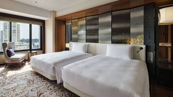 Quarto de hotel com duas camas, uma janela grande, uma cadeira e um painel de cabeceira decorativo.