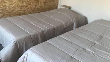Dos camas con ropa de cama gris en una habitación con pared de madera y un enchufe.