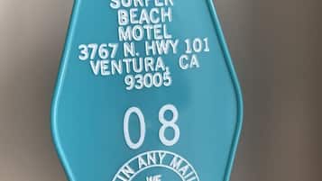A turquoise key tag with the text "SURFER BEACH MOTEL, 3767 N. HWY 101, VENTURA, CA 93005, 08, POSTAGE GUARANTEE".