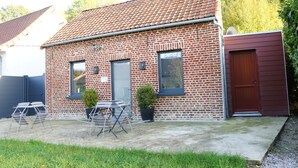 Une maison en briques avec un toit en tuiles, une porte d’entrée et un petit jardin agrémenté d’une table et de chaises.