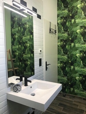 Une salle de bain avec un lavabo blanc, un miroir et un mur orné d’un motif végétal vert.