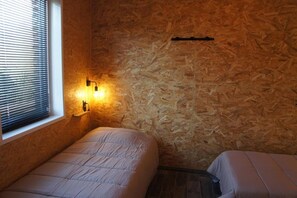 Une pièce avec un mur en bois, une fenêtre avec des stores et un lit recouvert d’une courtepointe.