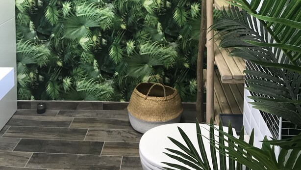 Une salle de bain avec un mur orné d’un motif de feuilles vertes, un banc en bois et une plante en pot.