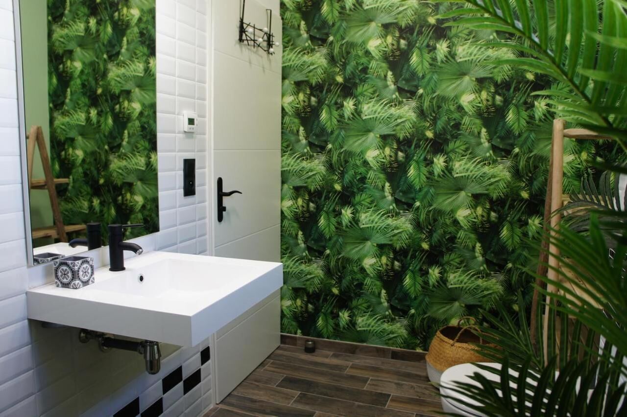 A bathroom with a white sink, a mirror, and a wall covered in a green leafy wallpaper.