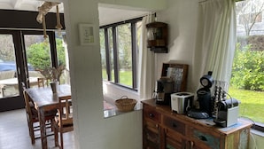 A cozy kitchen with a dining area, wooden cabinets, a coffee machine, and a view of the garden. - Family-friendly, cozy accommodation with a beautiful garden plot  (Bruinisse)
