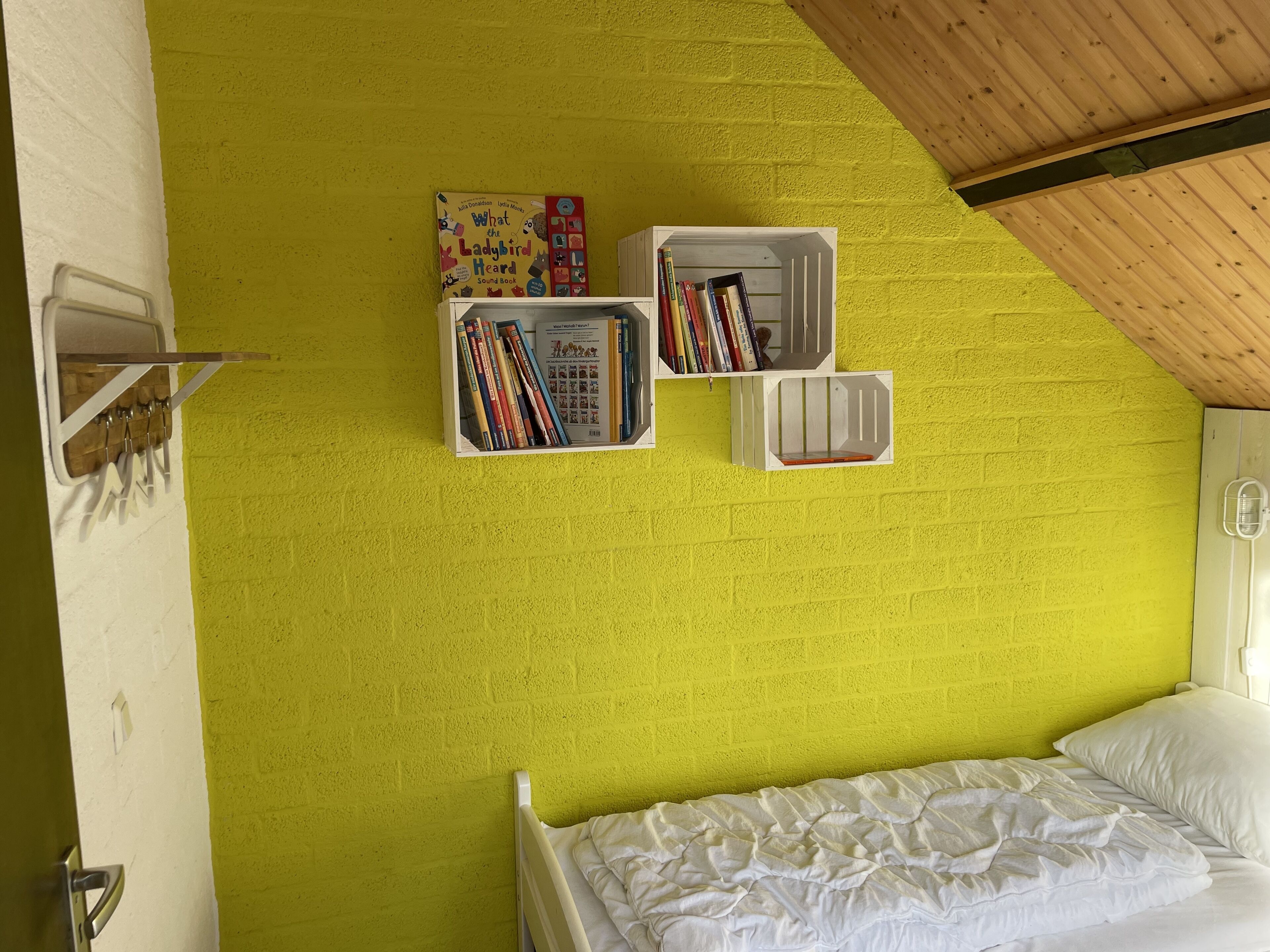 A room with a bright yellow brick wall, a white bed with white bedding, and two white bookshelves filled with books.