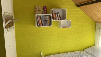 A room with a bright yellow brick wall, a white bed with white bedding, and two white bookshelves filled with books.