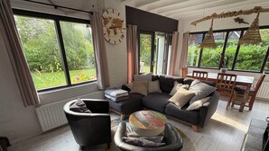 A modern living room with a sectional sofa, a round coffee table, and a dining area with wooden chairs. - Family-friendly, cozy accommodation with a beautiful garden plot  (Bruinisse)