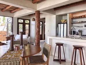 A spacious dining area with a wooden table and chairs, a kitchen with modern appliances, and large windows allowing natural light.