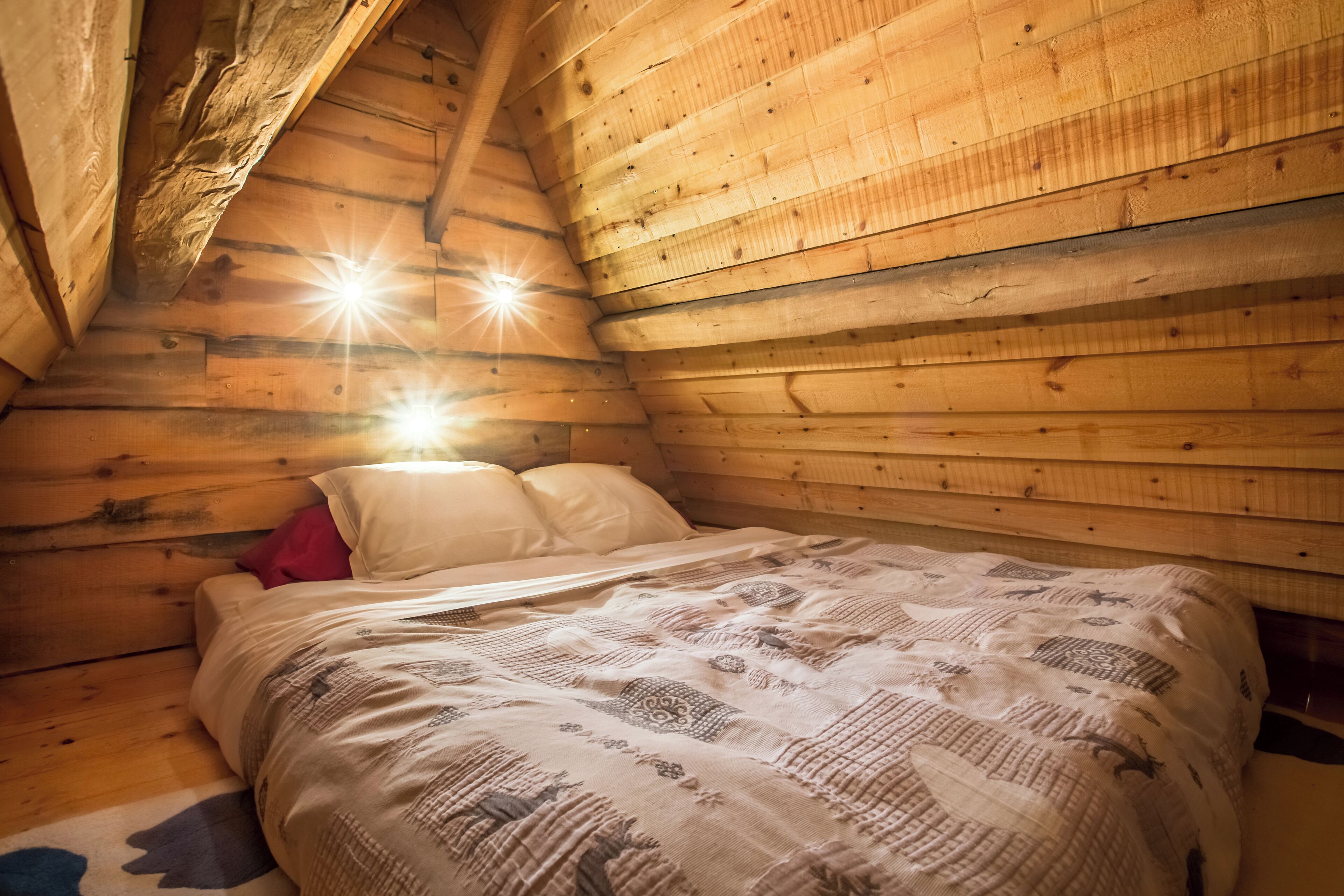 A cozy wooden cabin bedroom with a bed, pillows, and a rug.