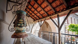Un espacio de estar al aire libre con encanto, con mesa y bancos de madera, un farol de metal decorativo, y una vista de un edificio con arcos al fondo.
