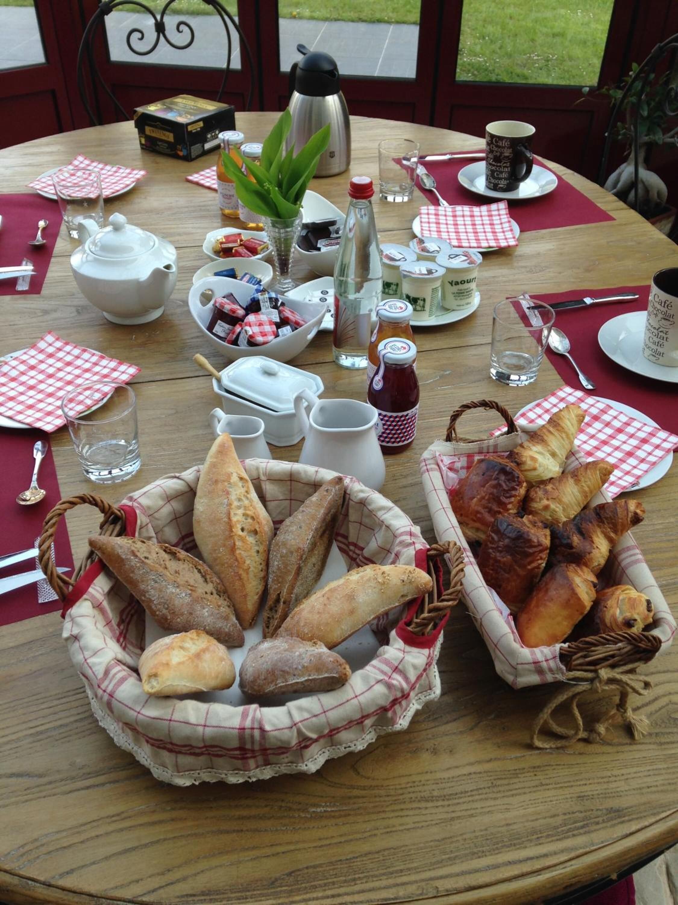 A round wooden table set for a meal with bread, condiments, and a teapot.