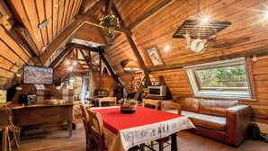 Interior acogedor de una cabaña con una mesa de comedor, sillas de madera, un sofá y un ventanal grande.