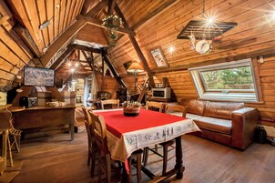 Interior acolhedor de uma cabana com uma mesa de jantar, cadeiras de madeira, um sofá e uma grande janela.