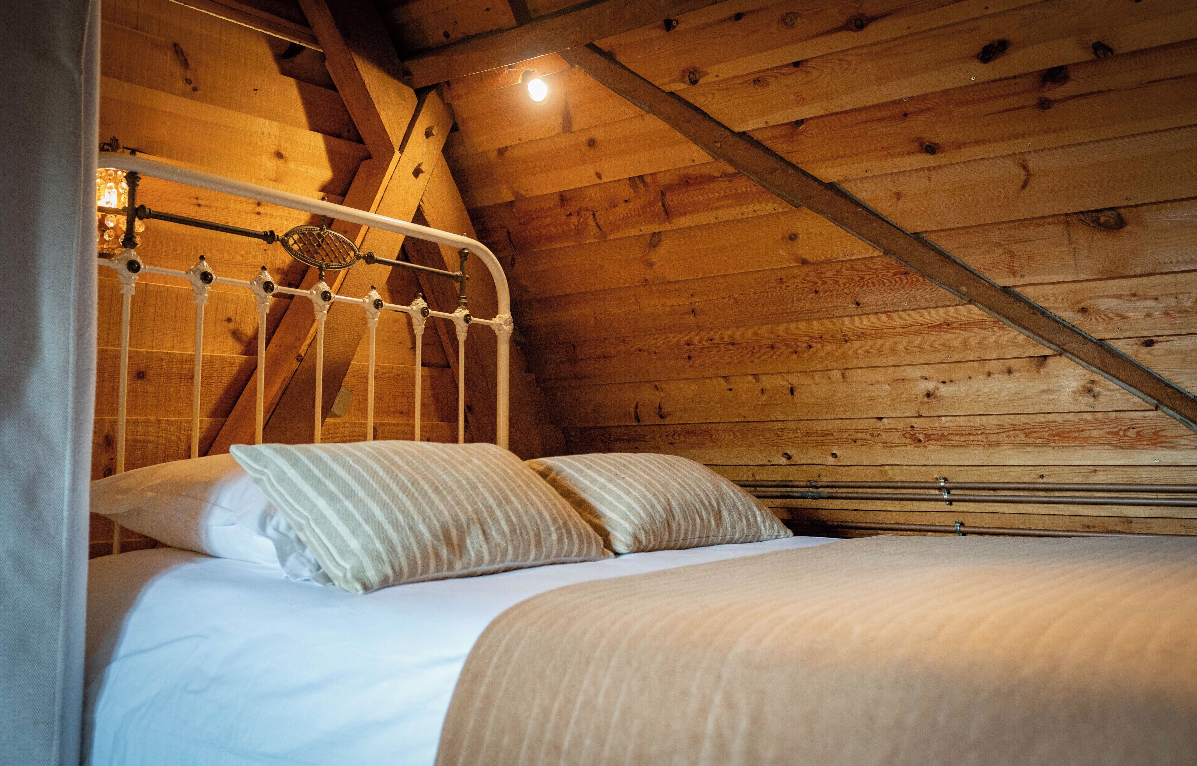 A wooden ceiling with a sloped design, a metal bed frame, and a white bedspread.