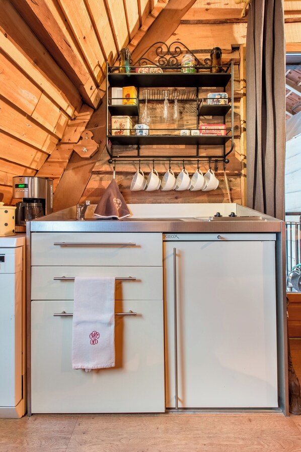 Una cocina compacta con estufa integrada, cafetera y un estante con utensilios de cocina.