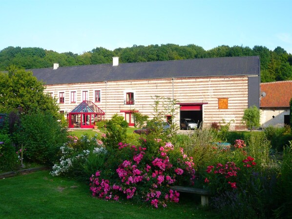 A large, rectangular building with a flat roof, surrounded by a well-maintained garden with various flowering plants and a gazebo. - La Ferme des Templiers (Enquin-lez-Guinegatte)