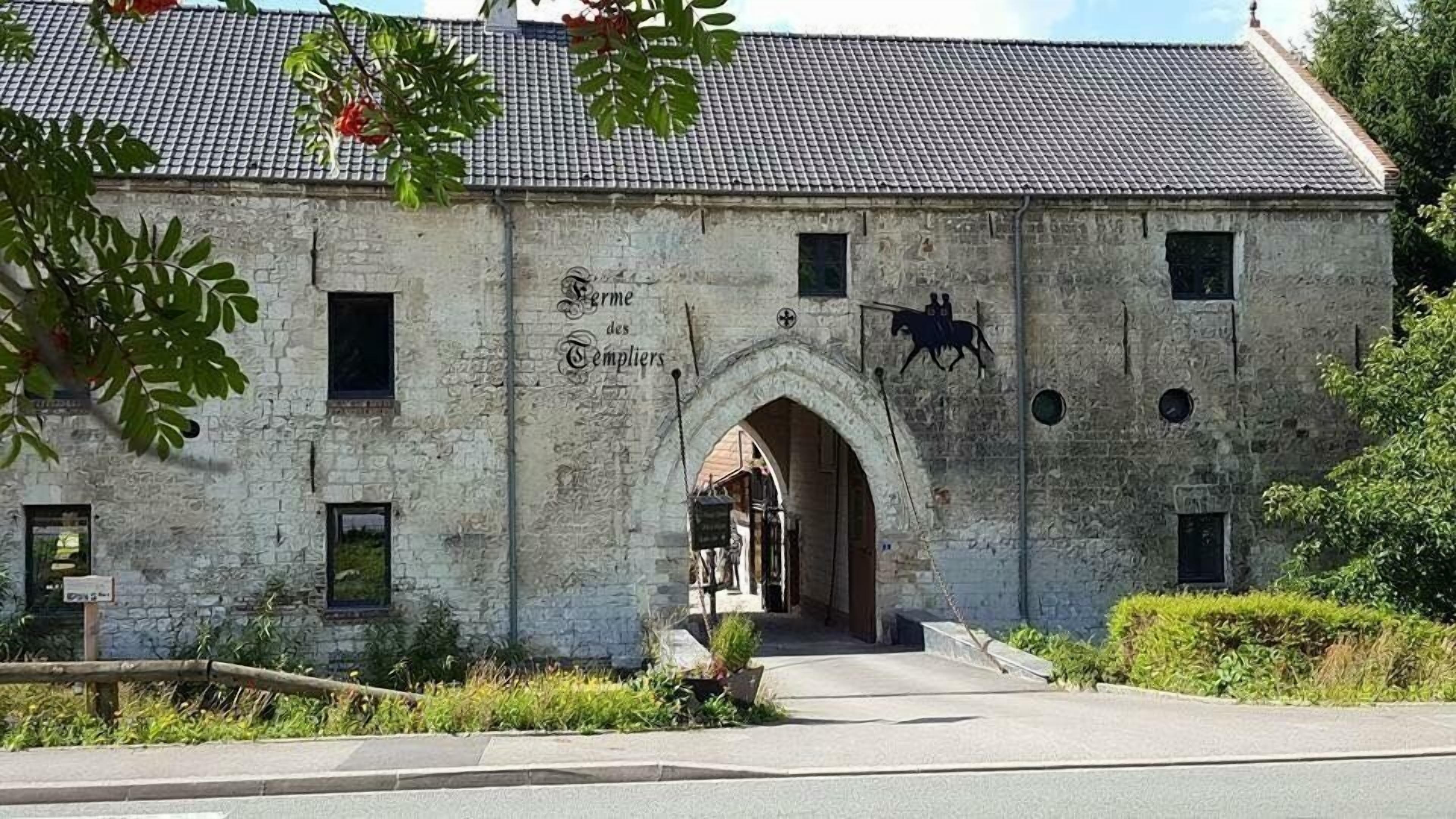 A stone building with a tiled roof, an arched entrance, and a silhouette of a horse on the wall.