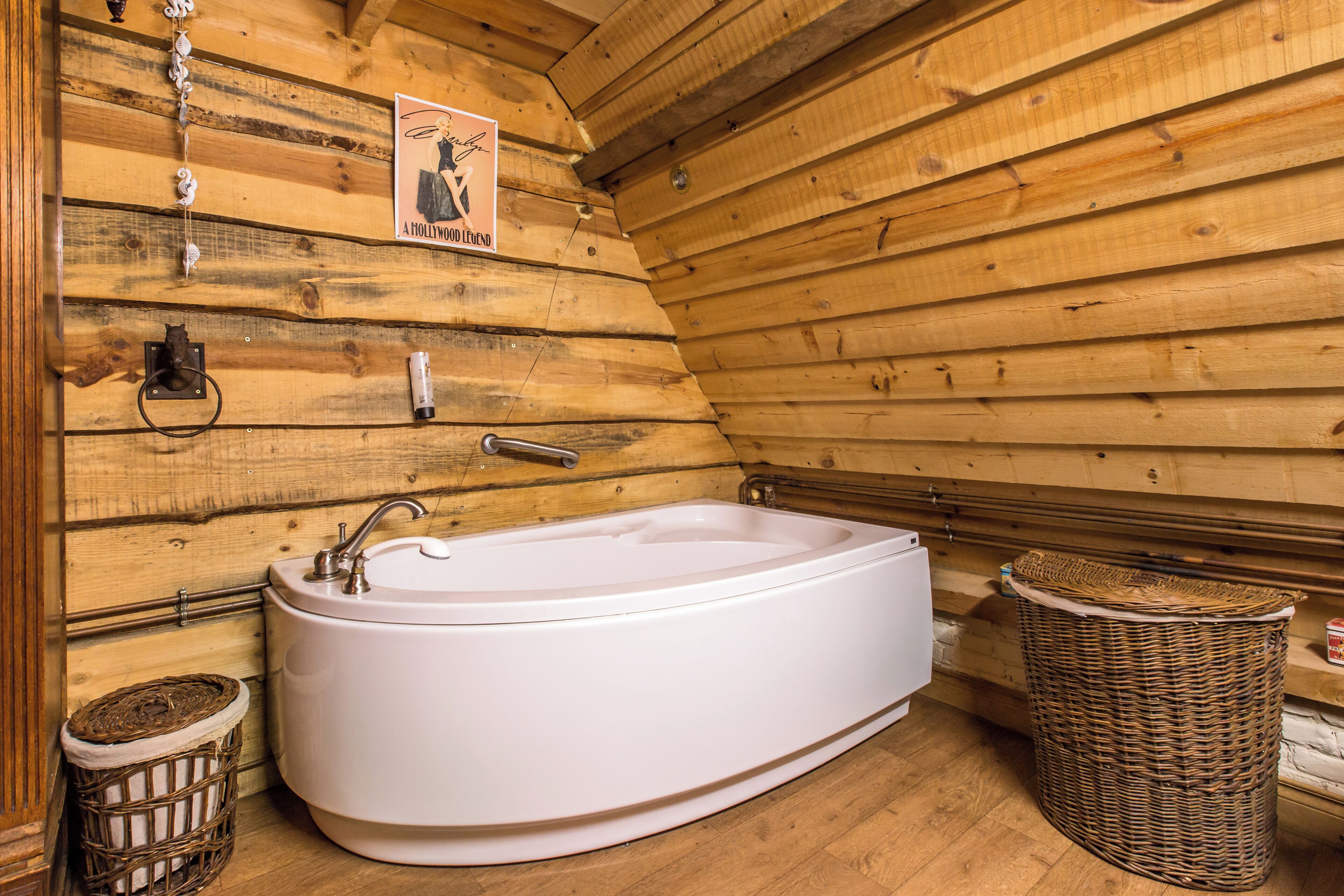 A wooden cabin interior with a white bathtub, a wicker basket, and a poster on the wall.