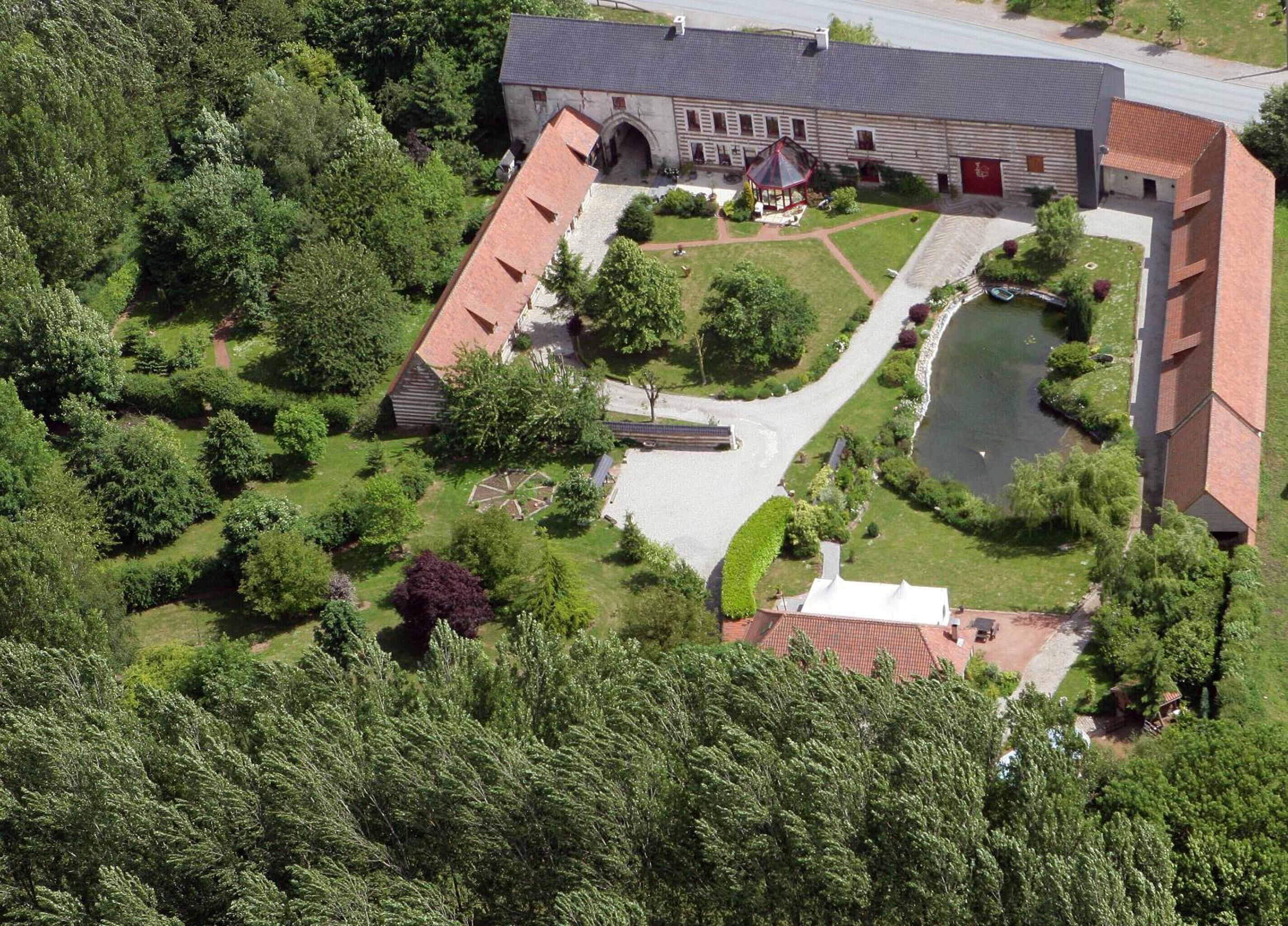 Luchtbeeld van een gebouw met een binnenplaats, een kleine vijver en omliggend groen.