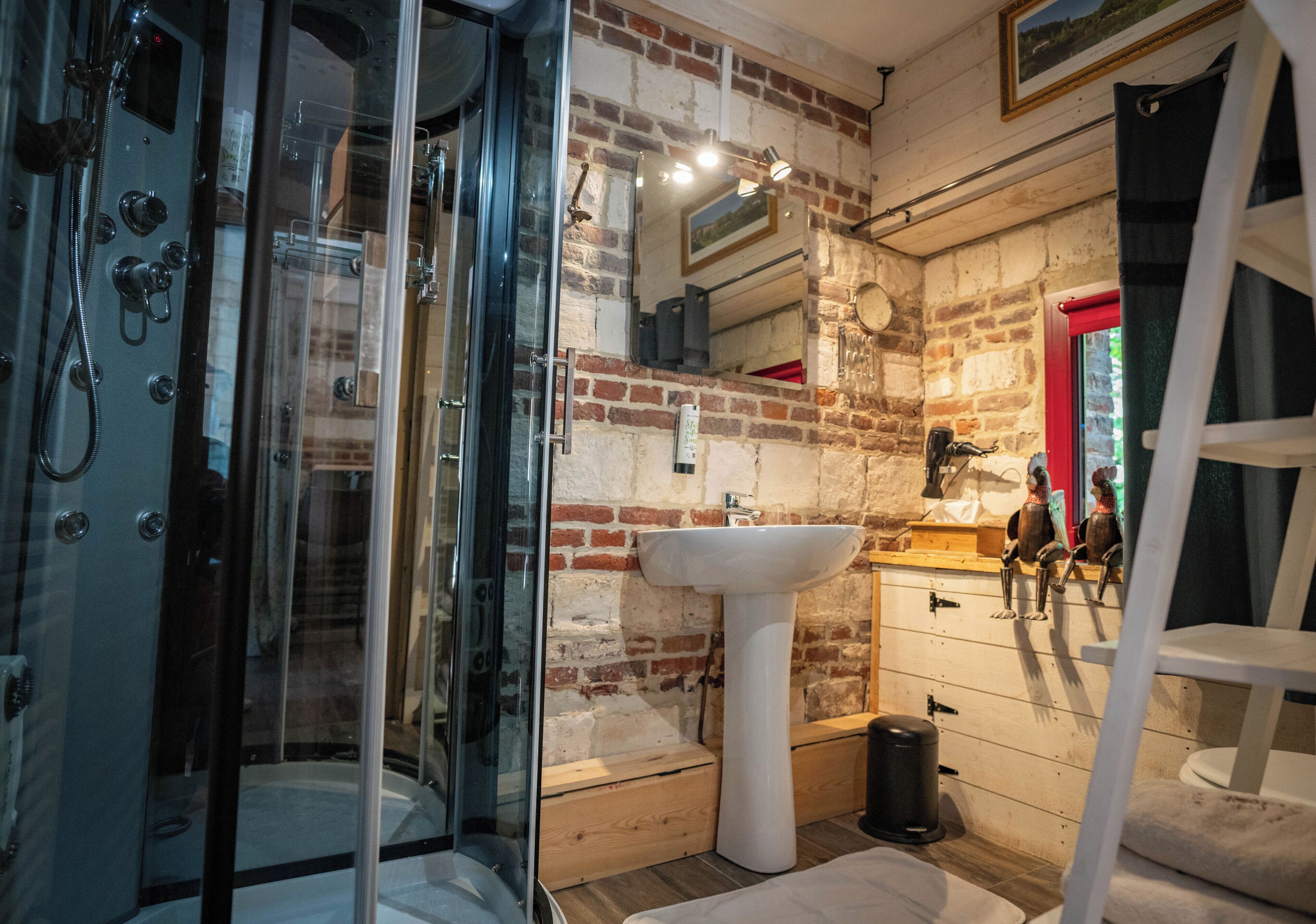 A bathroom with a glass-enclosed shower, a white pedestal sink, and a brick wall.