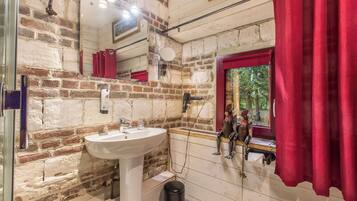 A bathroom with a white sink, red curtains, a window with a view of trees, and a rustic brick wall.