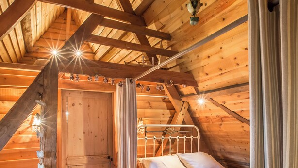 Un dormitorio acogedor en el ático, con techo de madera, cama con sábanas blancas y una puerta de madera rústica.