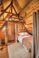 Um quarto de sótão aconchegante com teto de madeira, uma cama com roupa de cama branca e uma porta de madeira rústica.