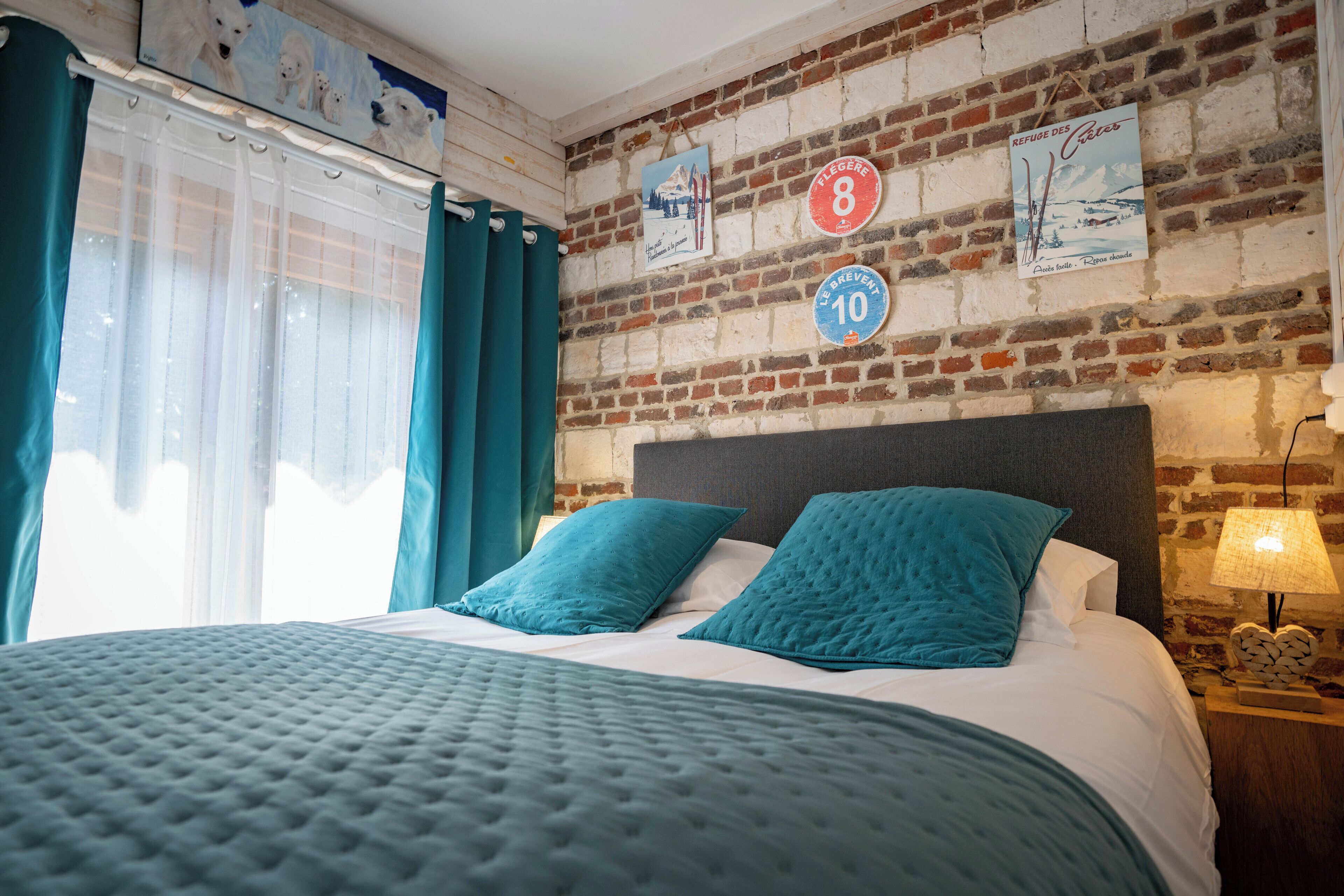 Ein Hotelzimmer mit Backsteinwand, einem Bett mit petrolfarbener Bettwäsche und einem Nachttisch mit Lampe.
