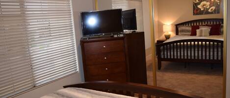 A bedroom with a bed, a dresser, a television on top, a ceiling fan, and a painting on the wall.