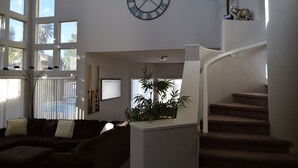 Ein geräumiger Wohnbereich mit großem Fenster, einer Treppe und einer Wanduhr.