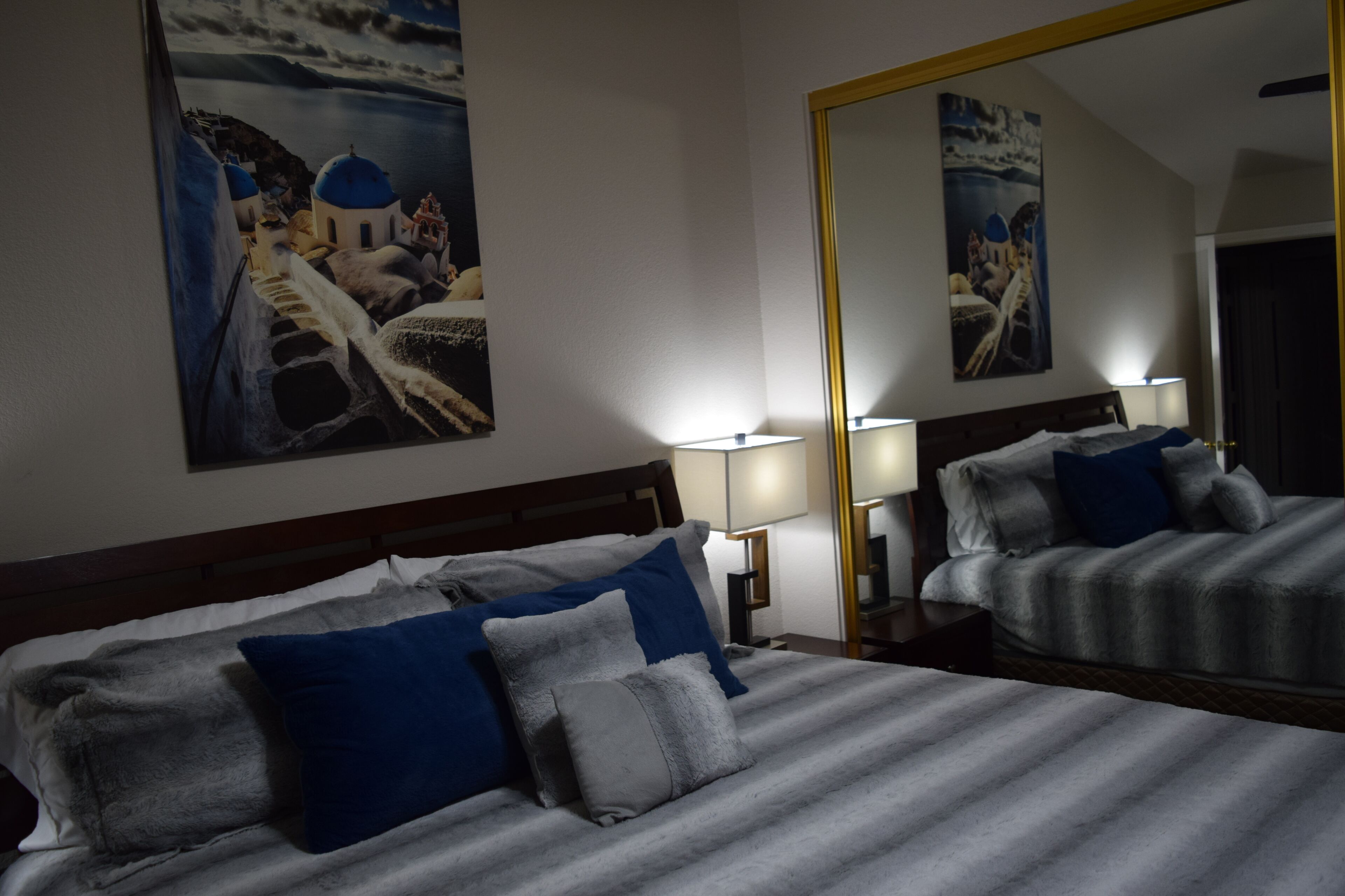 Hotellihuone, jossa on suuri sänky, kaksi yöpöytävalaisinta ja suuri peili, joka heijastaa huonetta.