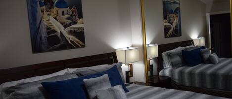 Hotellihuone, jossa on suuri sänky, kaksi yöpöytävalaisinta ja suuri peili, joka heijastaa huonetta.