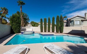 Une piscine entourée de chaises longues, bordée de grands arbres et surplombée par un ciel dégagé.