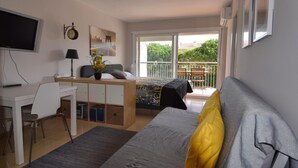 Ein Schlafzimmer mit Bett, Schreibtisch, Stuhl, Fernseher, Deckenventilator, Fenster und Balkon.