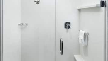 Une douche moderne dotée d’une porte en verre, d’un pommeau de douche à main, d’un siège intégré et d’un porte-serviettes.