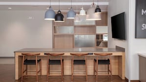 A modern kitchen with a central island, bar stools, pendant lights, and a flat-screen TV.