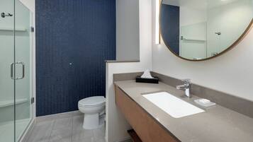 A modern bathroom with a glass shower enclosure, a white toilet, a beige vanity with a mirror, and a blue textured wall.