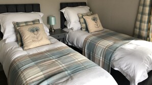 Hotellihuoneessa on kaksi sänkyä, joissa kummassakin on samanlaiset pääty ja tyyny. Sänkyjen välissä on yöpöytä, jonka päällä on lamppu.