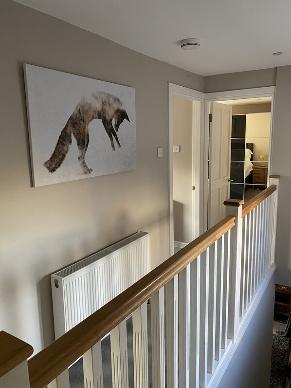 A staircase with a wooden handrail, a white radiator, and a painting of a wolf on the wall. - Garron House (Auchterarder)