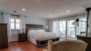 A bedroom with a large bed, bedside tables, a bench, and a view of the outdoors.