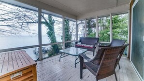 A covered outdoor area with a wooden table, two wicker chairs, and a glass table.