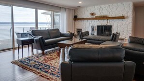 A modern living room with a stone fireplace, leather sofas, a coffee table, and a view of the water.