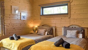 A room with two beds, each with a headboard, a window, and a bedside table with a lamp. - Birch Lodge - UK30006 (Mascalles, near Ulverston)