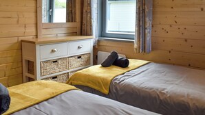 A wooden cabin room with two beds, a dresser, and a window with curtains.