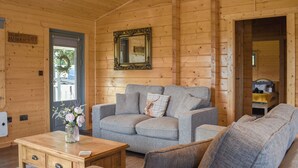 A cozy log cabin interior with a grey sofa, a wooden coffee table, and a mirror on the wall. - Birch Lodge - UK30006 (Mascalles, near Ulverston)