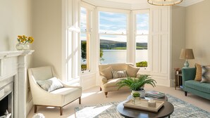 Una sala de estar acogedora con chimenea, un ventanal con vistas a un lago, un sofá verde y una mesa de centro.
