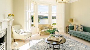 Un salón espacioso con chimenea, un sofá verde, un sillón color beige y una mesa de centro.