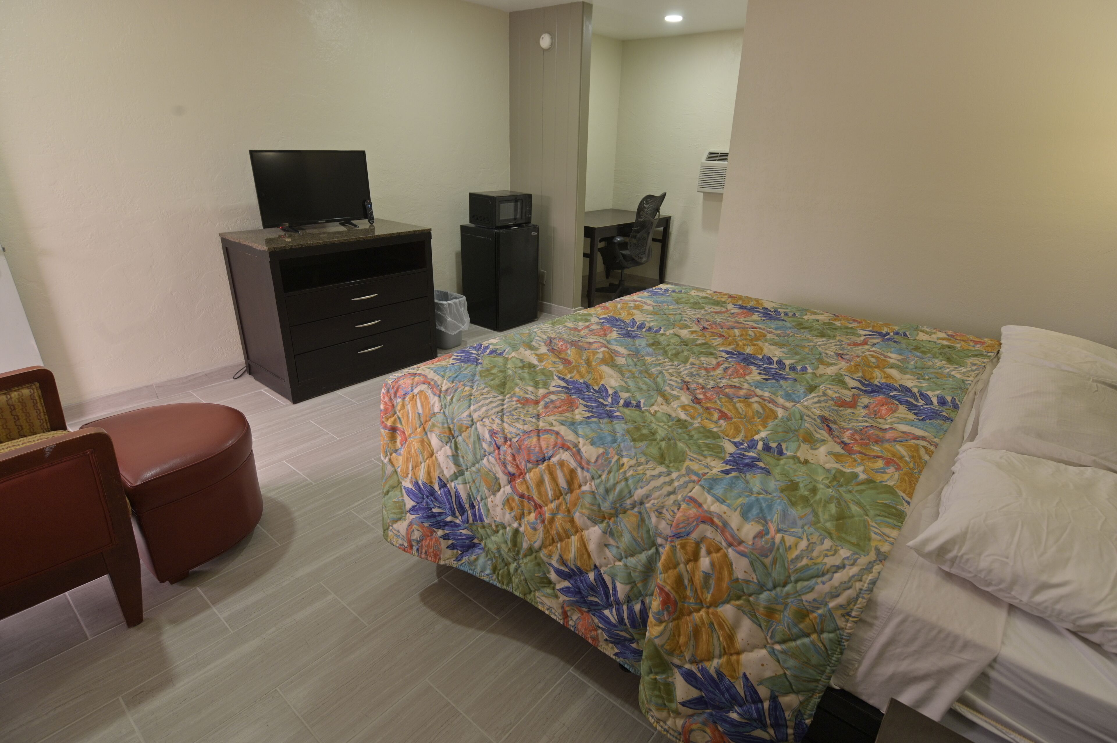 Un dormitorio con cama, escritorio, silla, televisor y refrigerador.