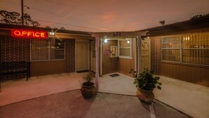 A building with a neon 'OFFICE' sign, a door labeled '601', and potted plants at the entrance. - Deluxe Inn (Bunnell)